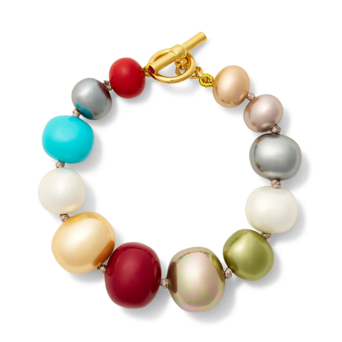 The CC & CO BY CATHERINE CANINO - RAINBOW PEBBLE BRACELET showcases large, irregular multicolored beads paired with a gold toggle clasp, arranged in a circle on a white background—handmade jewelry from NYC inspired by a playful rainbow bracelet aesthetic.