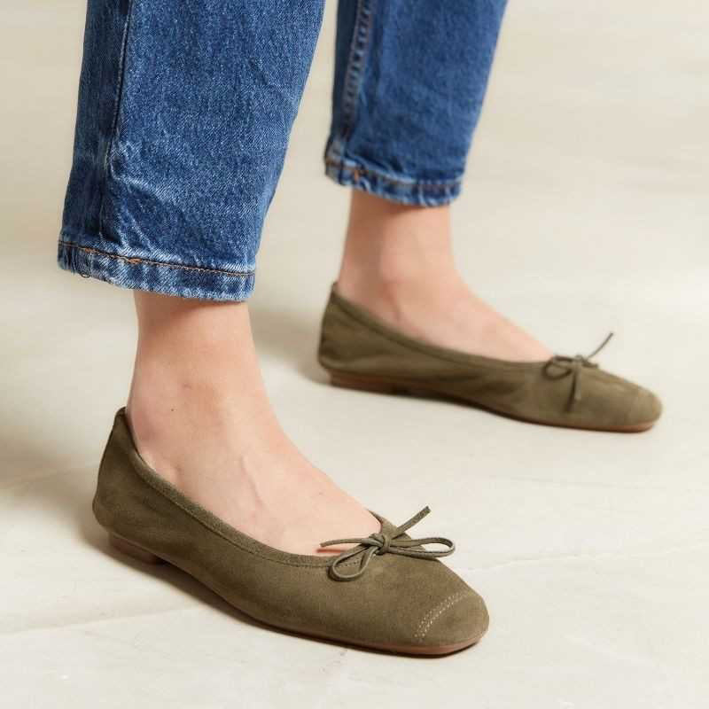 The REQINS - HARMONY suede ballerina flat in olive features a small bow on the toe, flat heel, and simple stitching, shown against a plain light background.