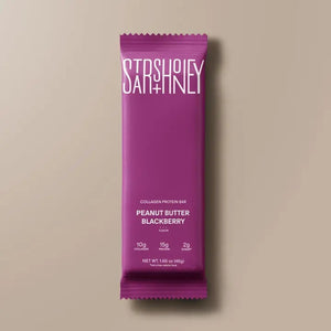 A purple STARS+HONEY - PEANUT BUTTER BLACKBERRY protein bar rests on a beige surface, with its wrapper highlighting 10g collagen, 15g protein, and 2g sugar.