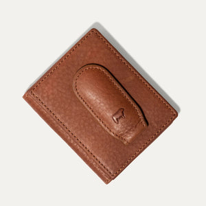 The WILL LEATHER GOODS Classic Money Clip sits atop an open full-grain leather wallet, both in brown, showcasing card slots against a plain light background.