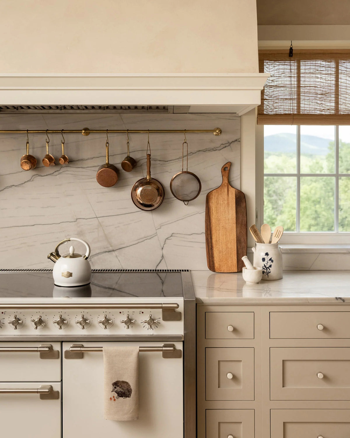 A HEDGEHOG WITH MUSHROOMS LINEN TEA TOWEL by CORAL & TUSK hangs from the handle of a white stove in a kitchen.