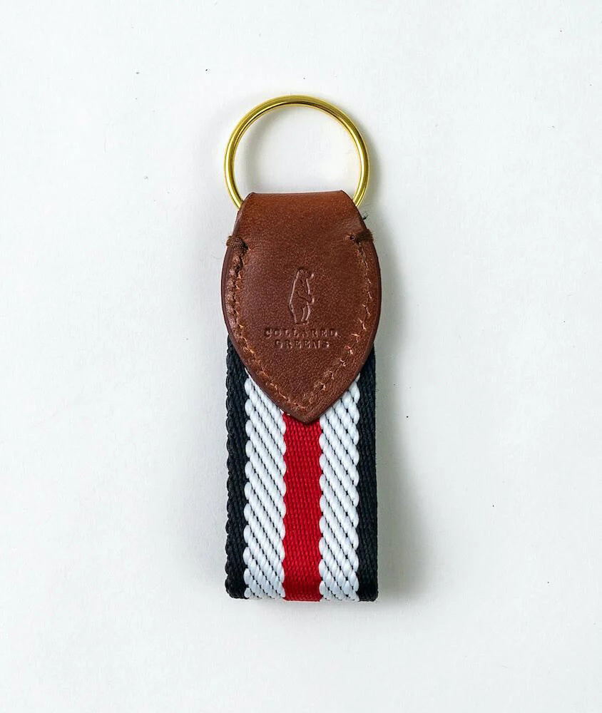 The COLLARED GREENS - DOCKSIDE KEY CHAIN IN RED WHITE BLACK by BIRD DOG BAY features a gold ring, brown embossed leather top, and a fabric strap with black, white, and red stripes for a stylish, functional touch.