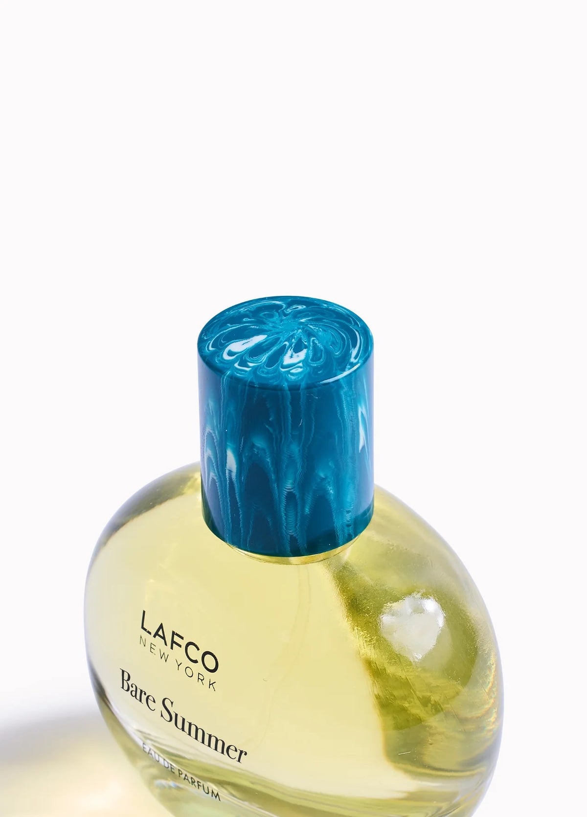 The LAFCO - FINE FRAGRANCE, BARE SUMMER 50ML perfume bottle, featuring a blue cap and displayed alongside delicate grasses, showcases its fresh and uplifting scent inspired by the sea and sand dunes. The text highlights opening, heart, and base fragrance notes that evoke the essence of summer. This vegan scent from LAFCO offers a clean, natural allure perfect for warm days.