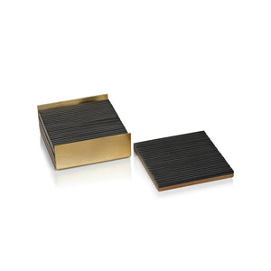 A set of RIBBED BONE COASTERS S4 by ZODAX, highlighting black-striped coasters neatly arranged in a gold metallic holder, with one coaster placed outside. The 4 in x 4 in coasters and holder showcase a modern, sleek design and are displayed on a white surface.