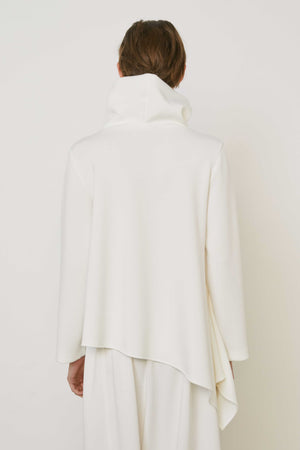 A person with brown hair faces away wearing the MEIMEIJ ASYMMETRICAL COWLNECK TOP in lightweight scuba fabric, featuring an asymmetrical hem, paired with matching white bottoms, against a plain white background.