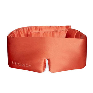 A person wearing a white tank top is lying on a pillow with the DROWSY - SATIN SLEEP MASK by DROWSY SLEEP CO covering their eyes. They look relaxed, enjoying beauty sleep as their hand rests gently on the pillow.