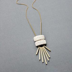 The DAVID AUBREY - WHITE GEOMETRIC PENDANT NECKLACE by DAVID AUBREY showcases two white magnesite beads above six gold-plated brass bars arranged like rays, all set against a simple gray background.