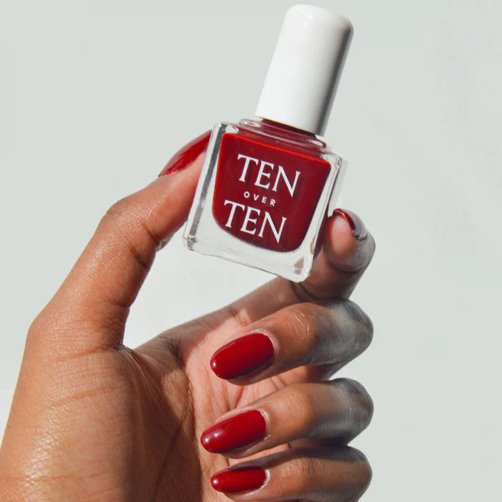 A glass bottle of TENOVERTEN - NAIL POLISH from the brand TEN OVER TEN, featuring a white cap and a dusty pink nail color. The front label displays "TEN OVER TEN" in white uppercase letters. This vegan, eight-free formula ensures both beauty and peace of mind. The background is plain and light-colored.