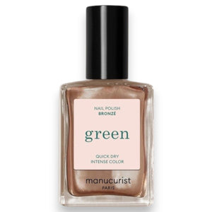 A hand with shimmery bronze vegan, cruelty-free nail polish holds a matching bottle labeled “MANUCURIST - GREEN™ Nail Polish in Tanned” against a brown sweater.