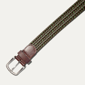 The WILL LEATHER GOODS - STRETCH BELT features a green, purple, and black braided design with full-grain leather accents by the silver buckle and tip, shown on a plain light background. Brand: WILL LEATHER GOODS.