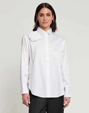 A person with short, brown hair is standing and facing away from the camera, wearing a HINSON WU - HALSEY LONG SLEEVE COTTON SATIN SHIRT WITH FLOWER. They have paired this black button-up shirt, made of a cotton and spandex blend, with light-colored pants. The background is plain and light-colored.