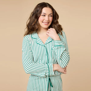 A woman wears the SOFTIES ARIA SLIM NOTCH COLLAR PJ SET, featuring a long-sleeved button-down top and matching wide-leg pants in red and white vertical stripes with red piping details.