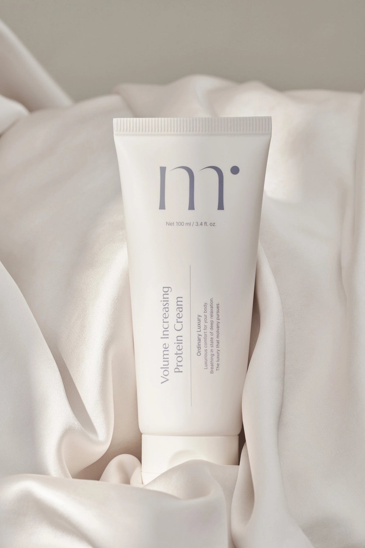 A white tube labeled &quot;MOLVANY - VOLUE IMPACT PROTEIN CREAM&quot; infused with colostrum protein for skin elasticity, stands before its box. The minimalistic packaging has blue text on a clean background, with &quot;HONG CHEON USA, INC&quot; printed at the top.