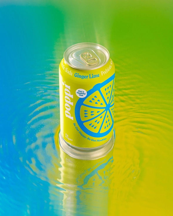A yellow can of POPPI - GINGER LIME prebiotic soda features blue lemon slice graphics, white and blue text, “For a Healthy Gut,” and 4g sugar. Infused with apple cider vinegar for digestive health, the can stands on a white background.