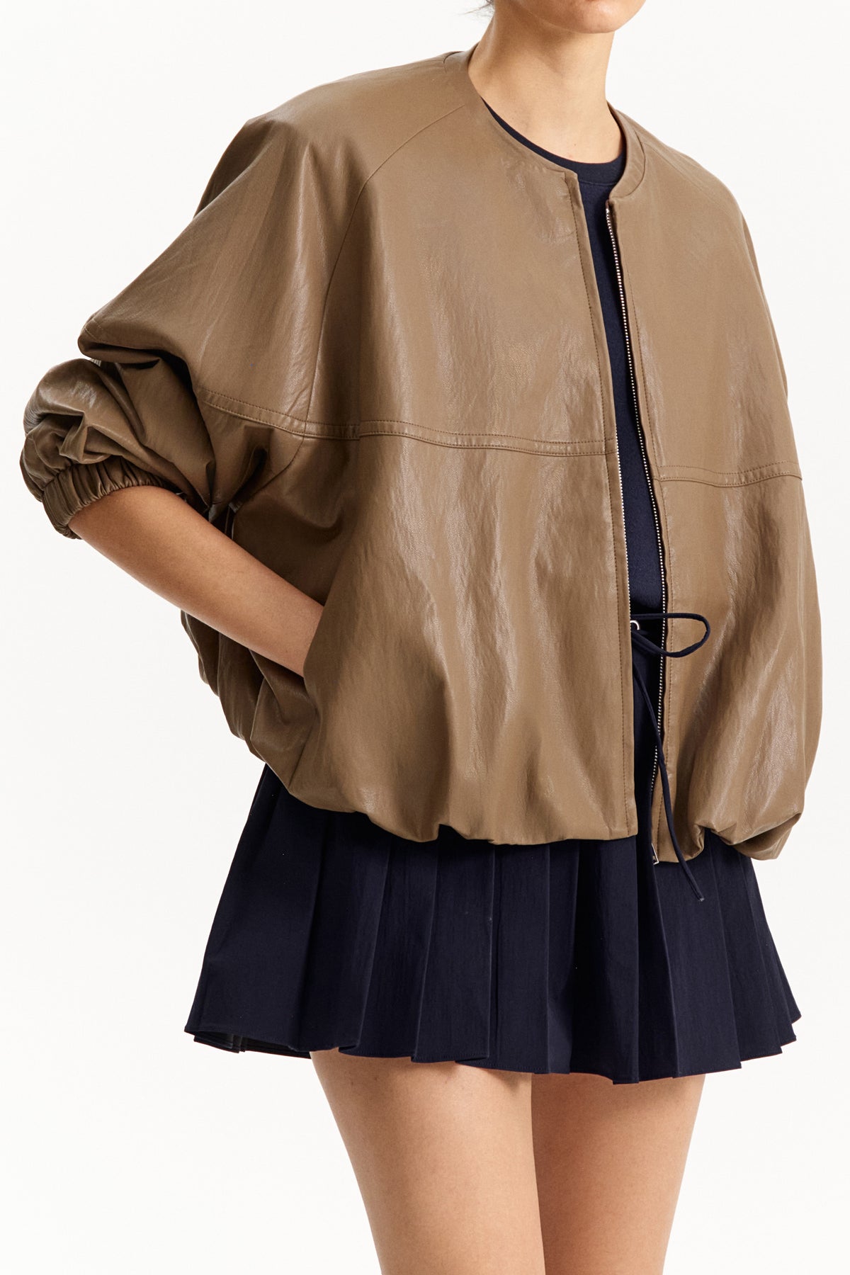 The ELEH - THE MOD BOMBER JACKET by ELEH is a brown leather jacket featuring a sculptural design, front zipper, round neckline, and long oversized sleeves with gathered cuffs, shown against a plain white background.