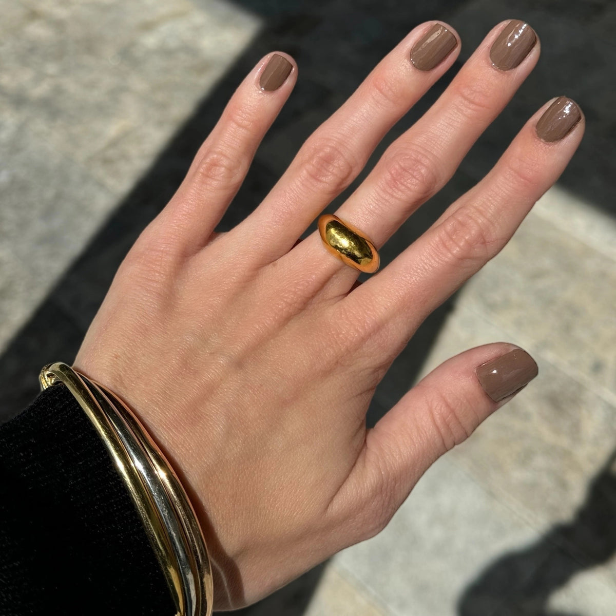 A hand with brown-painted nails holds a bottle of TEN OVER TEN WARREN NAIL POLISH, an 8-free polish by TEN OVER TEN, against a plain light background.