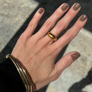 A hand with brown-painted nails holds a bottle of TEN OVER TEN WARREN NAIL POLISH, an 8-free polish by TEN OVER TEN, against a plain light background.