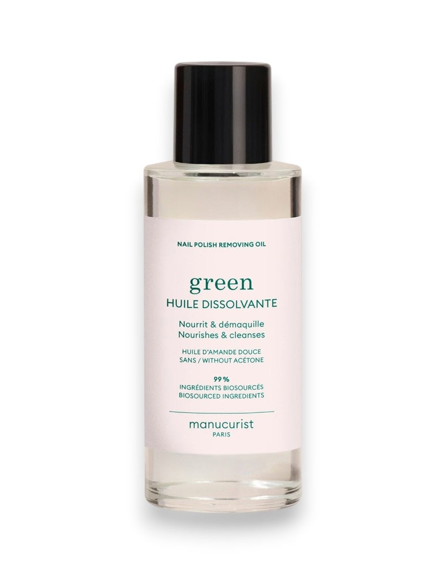 A clear bottle of MANUCURIST - GREEN NAIL POLISH REMOVING OIL by MANUCURIST INC, featuring a black cap and white label with green and blue text highlighting its nourishing, plant-based, acetone-free formula.