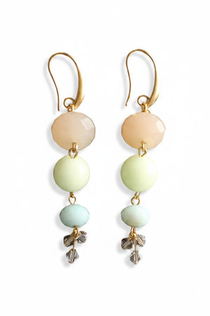 The DAVID AUBREY - JADE AND GLASS EARRINGS by DAVID AUBREY feature three vertically stacked pastel beads in peach, pale yellow, and mint green hues on gold-plated ear wires, finished with delicate crystal flower charms. These jade and glass earrings are showcased against a dark textured background.