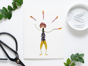 The JUGGLE GREETING CARD by PETAL PEOPLE PRESS showcases a whimsical figure crafted from pressed flowers on a white background, featuring a purple bloom head, green stem limbs, a body with purple blooms, and an orange petal halo—an enchanting piece of botanical art.