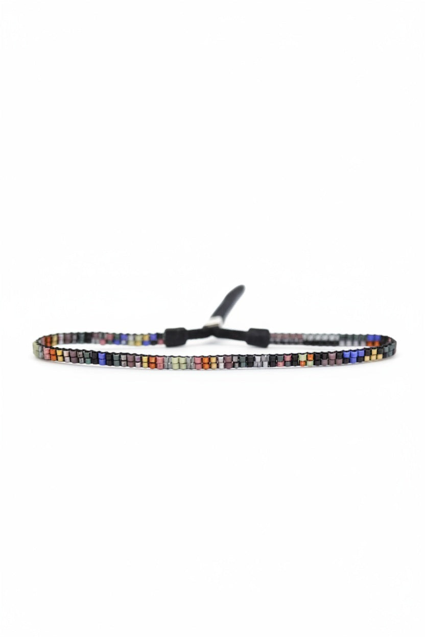 The JULIE ROFMAN - MINI BRACELET by JULIE ROFMAN JEWELRY is a vibrant handwoven piece adorned with small, square beads in various shades of pink, red, and white. It is displayed against a white background and includes a straightforward sterling silver clasp for convenient fastening.