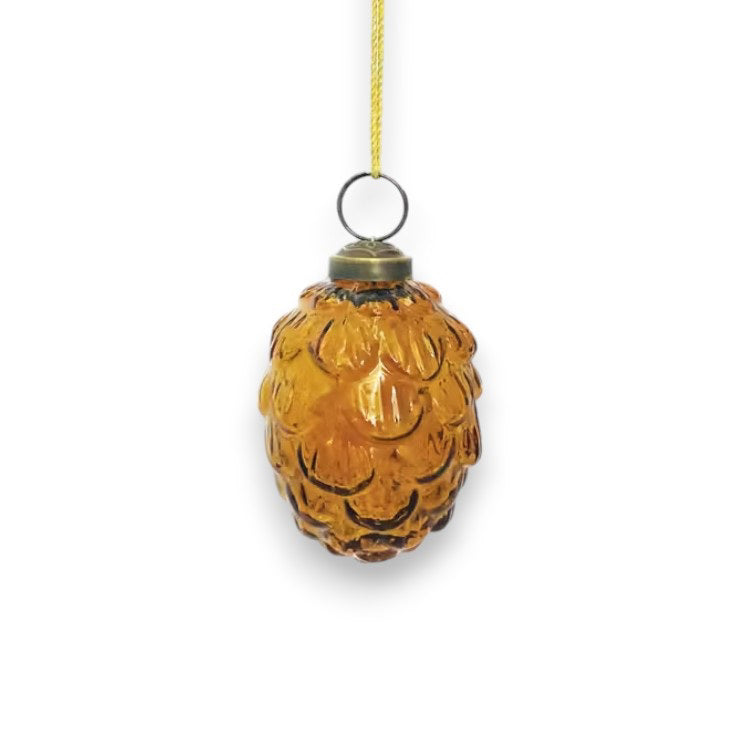 The Creative Co-op Glass Pinecone Ornament, with its amber hue and embossed texture, hangs elegantly from a yellow string against a crisp white background.