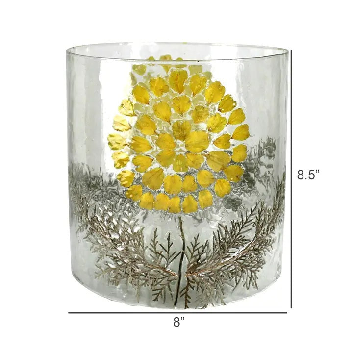 The HOMART ENAMEL HURRICANE WITH YELLOW FLOWER is a cylindrical glass vase featuring pressed yellow petals and green ferns in the design, perfect as a unique garden luminary.