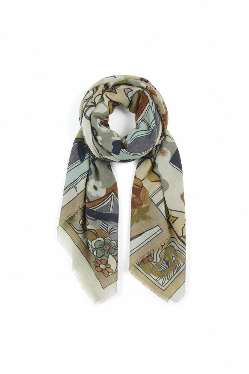 The STORIATIPIC - GAYA Wool Scarf in Beige by STORIATIPIC is a lightweight wool and silk scarf featuring a floral and geometric pattern in muted green, beige, orange, and navy tones, shown loosely knotted against a plain white background.