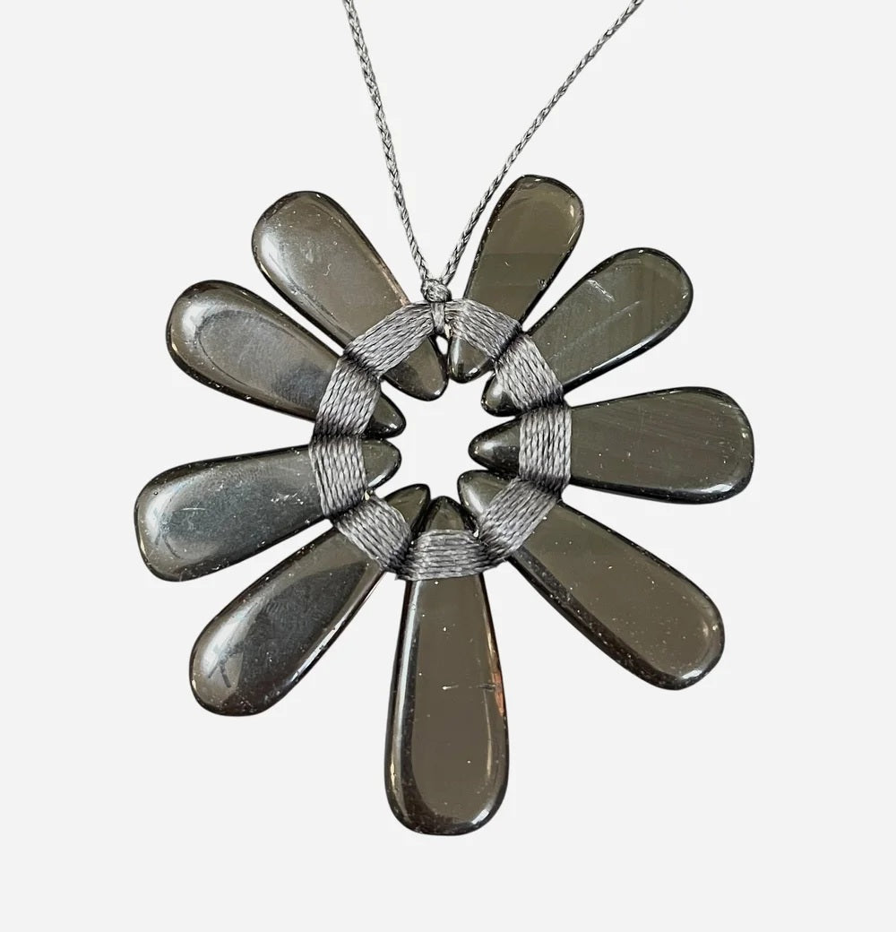 A mannequin wears a shaggy beige jacket paired with the ANN LIGHTFOOT Nine Petal Smokey Quartz Flower Necklace, which features a modern black cord and a bold, dark metallic floral pendant.
