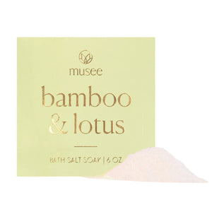 A MUSEE - Bamboo & Lotus Mini Bath Salt Soak from MUSEE rests on a white plate beside a green potted succulent, all arranged atop a wooden surface.