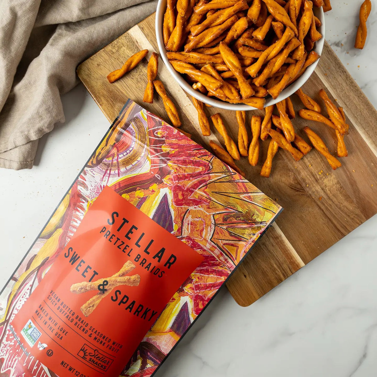 A vibrant bag of STELLAR SNACKS - SWEET &amp; SPARKY PRETZEL BRAIDS, showcasing bold red and orange abstract artwork, flavorful buffalo-inspired seasoning, and clear product information on the front—the ideal pick for those who love spicy snacks.
