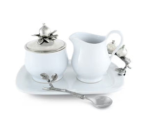 The VAGABOND HOUSE POMEGRANITE CREAMER SET includes a white ceramic sugar bowl with a metallic lid featuring pewter pomegranates, a matching cream pitcher, and a silver spoon with branch-like handle and pomegranate accents on a rectangular tray.