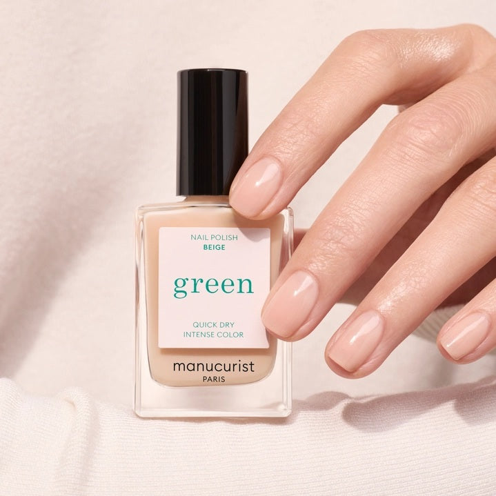 A hand with neatly manicured nails—polished in Beige with MANUCURIST - GREEN™ NAIL POLISH by MANUCURIST INC—rests gently on a textured, cream-colored, ruffled sweater.