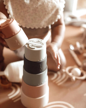 Introducing the LARGE SILICONE STACKING CUPS by ALI + OLI, a delightful collection of neutral and pastel-colored cups designed to promote fine motor skills. This baby development toy includes various numbered cups from 1 through 6, with pieces shaped like flowers, animals, a cactus, and a rainbow. Each cup can be nested or stacked vertically for endless fun and learning.