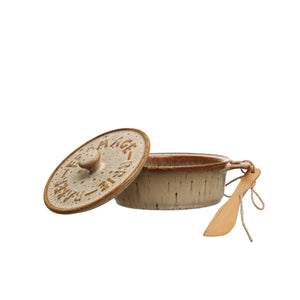 A Brie cheese sits in the CREATIVE COOP STONEWARE BRIE BAKER WITH LID AND BAMBOO SPREADER, topped with pear and honey. The lid is set aside, while a bamboo spreader and half a pear rest nearby on parchment paper.