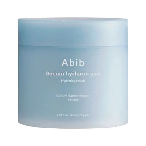 A light blue cylindrical container labeled "SEDUM HYALURON PAD HYDRATING TOUCH" by ASIAN BEAUTY WHOLESALE, featuring Sedum Sarmentosum Extract, hyaluronic acid, and containing 60 hydrating toning pads.