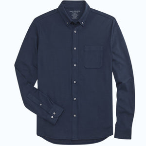 A man with short dark hair wears the MACK WELDON Silver Pique Long Sleeve Button Up Shirt in True Navy, standing against a plain light background with a neutral expression and his hands together in front of him.