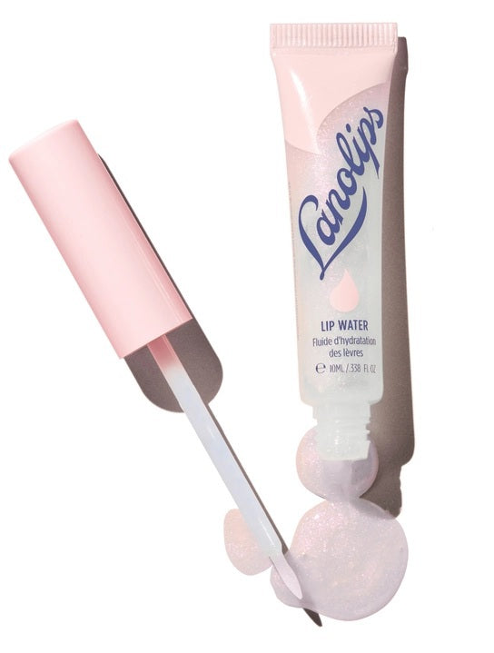 A close-up of a person smiling with glossy pink lips—enhanced by LANOLIPS - LIQUID LANOLIN LIP WATER from LANOLIPS—and smooth brown skin against a light blue background.