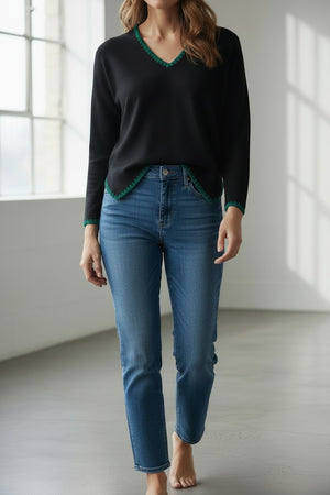 A person with light blonde hair stands sideways against a white background, wearing the MEIMEIJ V Neck Hi Low Top with embroidered contrast stitch detail by MEIMEIJ, paired with white pants.