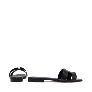 The image depicts the MICHELE LOPRIORE - H SLIDE, a single brown leather slide sandal with an open-toe design. The upper features two wide straps with geometric cutouts. The thin sole appears to be made of light brown wood-like material. Made in Italy by MICHELE LOPRIORE, the sandal is displayed against a plain white background.
