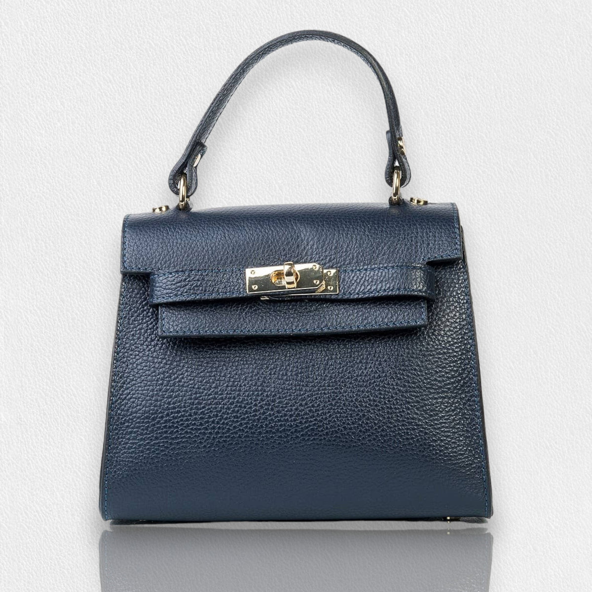 The LE BORSETTE LEATHER SATCHEL BAG is a small, structured satchel-shaped handbag in light pink, featuring a gold clasp at the front. It boasts a single top handle, an adjustable shoulder strap, and two gold-tone hardware pieces on either side of the handle. The textured leather adds to its luxurious and elegant appearance against the plain white background.