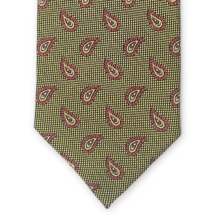 A close-up of the PETER-BLAIR - ALBEMARLE SILK TIE IN YELLOW by BIRD DOG BAY showcases a yellow and black houndstooth pattern, accented with evenly spaced red and pink paisley designs. Handmade in New York, this woven silk tie features an elegantly pointed tip.