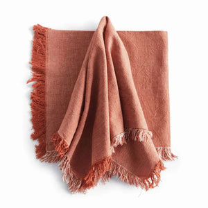 Four NAPA HOME AND GARDEN - AURA DINNER NAPKINS in rust, made of washable cotton with fringed edges, are neatly fanned out on a white surface.