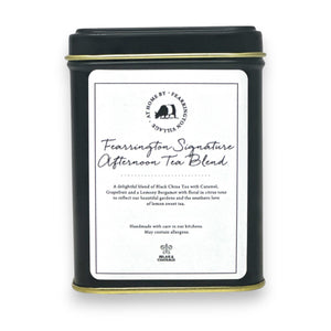 A black tin labeled "Fearrington Signature Afternoon Tea Tin" from the Fearrington House Signature Collection contains a luxurious blend of Loose Leaf Black China Tea with caramel, grapefruit, and lavender. The tin has a simple, elegant design accented by a white label featuring the product description.