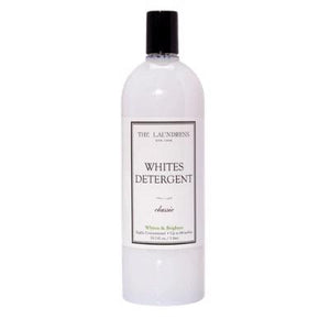 A tall, cylindrical bottle with a black cap is labeled "THE LAUNDRESS - WHITES DETERGENT 32OZ." The label also states "Classic" and highlights its versatile, all-purpose formula for cleaning white fabrics. With a bio-based formulation and a clean, minimalist design, the bottle embodies the brand's aesthetic.