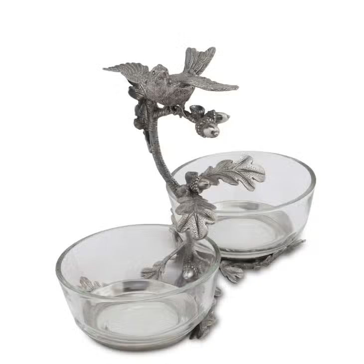 The VAGABOND HOUSE - SONG BIRD DOUBLE CONDIMENT BOWL features two glass bowls on an elegant metal stand adorned with ornate leaves and branches, topped by a pewter songbird.