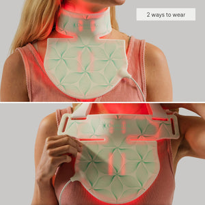 An OMNILUX - CONTOUR NECK & DECOLLETE KIT device by OMNILUX, featuring a white and pink pattern and designed for red light therapy, stands upright on a white surface with soft red light glowing around its edges.