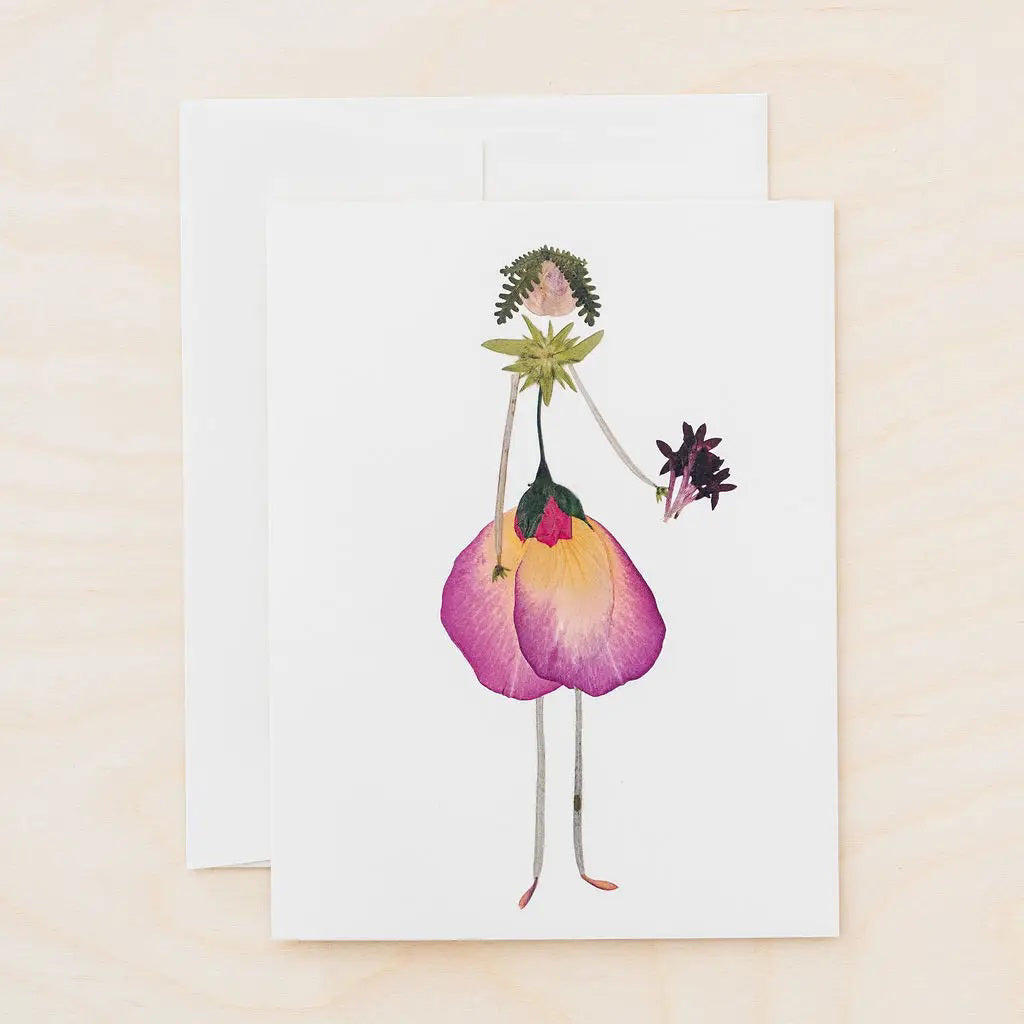The PETAL PEOPLE PRESS - THINKING OF YOU CARD by PETAL PEOPLE PRESS features a person illustrated with pressed flowers and leaves, petals as a dress, and stems as arms and legs, displayed on a white table with greenery and crafting tools.