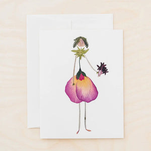The PETAL PEOPLE PRESS - THINKING OF YOU CARD by PETAL PEOPLE PRESS features a person illustrated with pressed flowers and leaves, petals as a dress, and stems as arms and legs, displayed on a white table with greenery and crafting tools.
