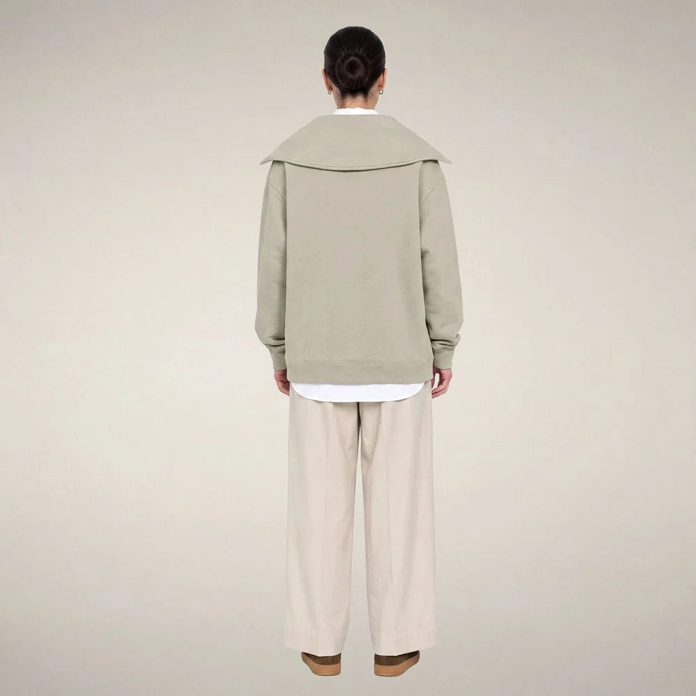 A woman wears a sleek rainy beige SAVE THE DUCK - HINATA HALF ZIP TOP with a wide collar and matching wide-leg drawstring sweatpants.